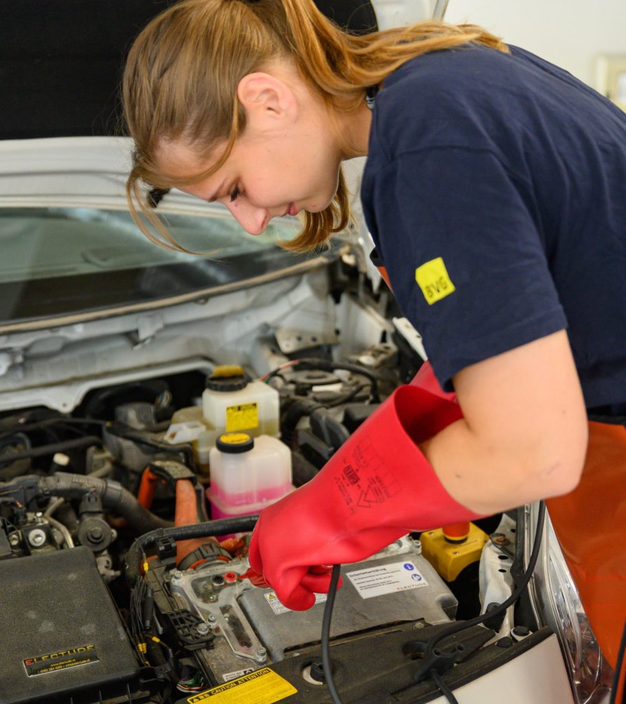 Auszubildende arbeitet an einem KFZ mit Hochvolttechnik